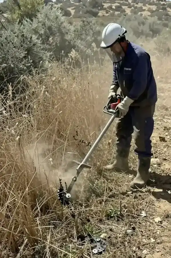 Εργάτης με θαμνοκοπτικό και μέσα προστασίας κόβει ξερή βλάστηση σε οικόπεδο